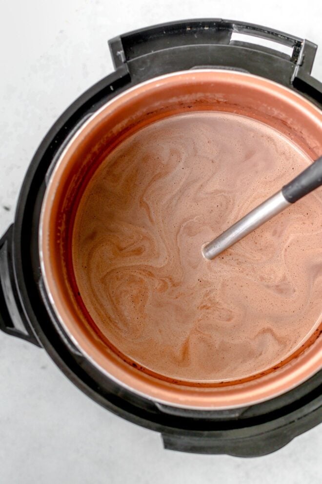 This is an overhead vertical image looking into an instant pot with hot cocoa in it. A ladle is in the instant pot with the handle leaning against the right side of it. The instant pot is on a light grey surface.
