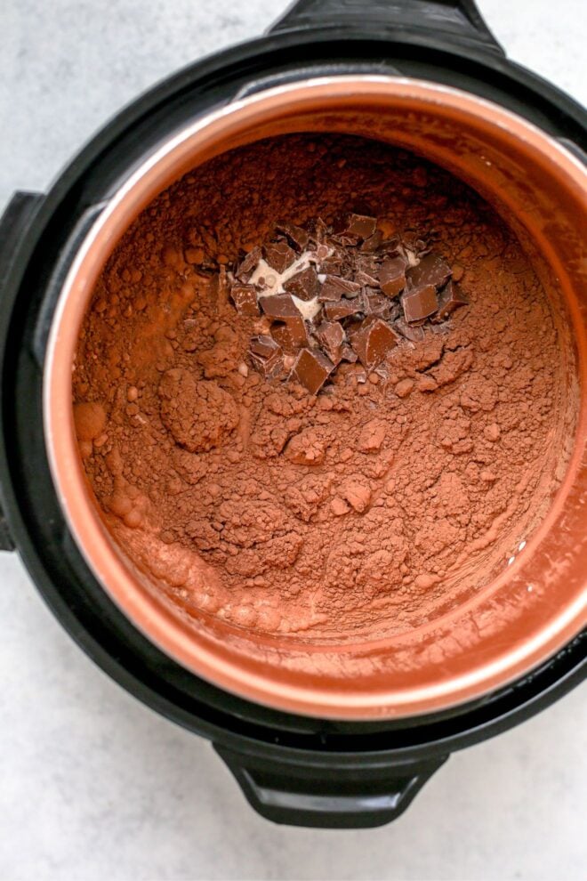 This is an overhead vertical image looking into an instant pot with cocoa powder, chopped chocolate and milk in it, not yet stirred or combined. The instant pot is on a light grey surface.