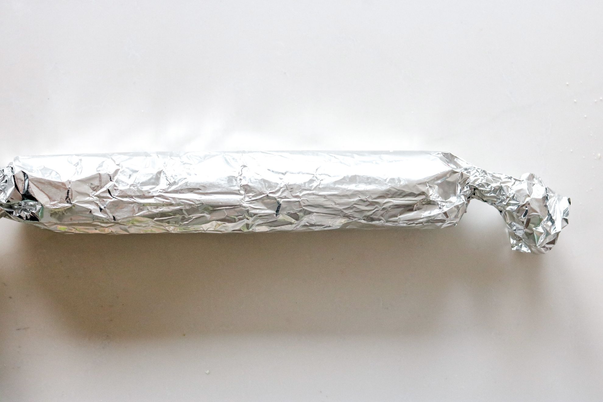 This is an overhead horizontal image of a tin foil wrapped log. The log sits on a white surface.