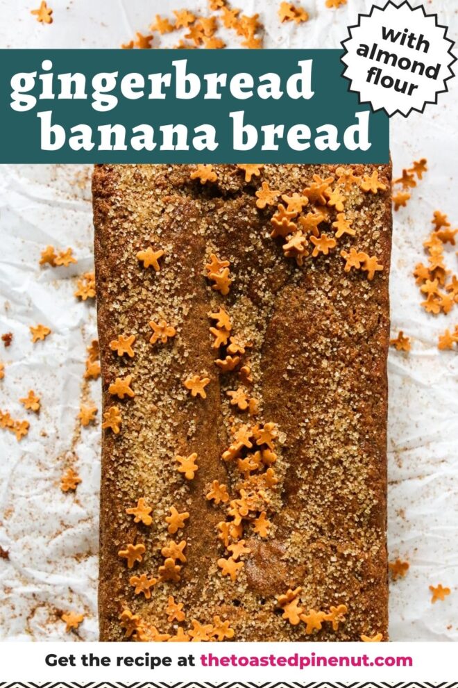 This is an overhead vertical image of a gingerbread loaf on a white piece of parchment paper. The loaf is topped with turbinado sugar and mini gingerbread men sprinkles. Text overlay reads "gingerbread banana bread with almond flour" at the top and "get the recipe at thetoastedpinenut.com" at the bottom of the image.