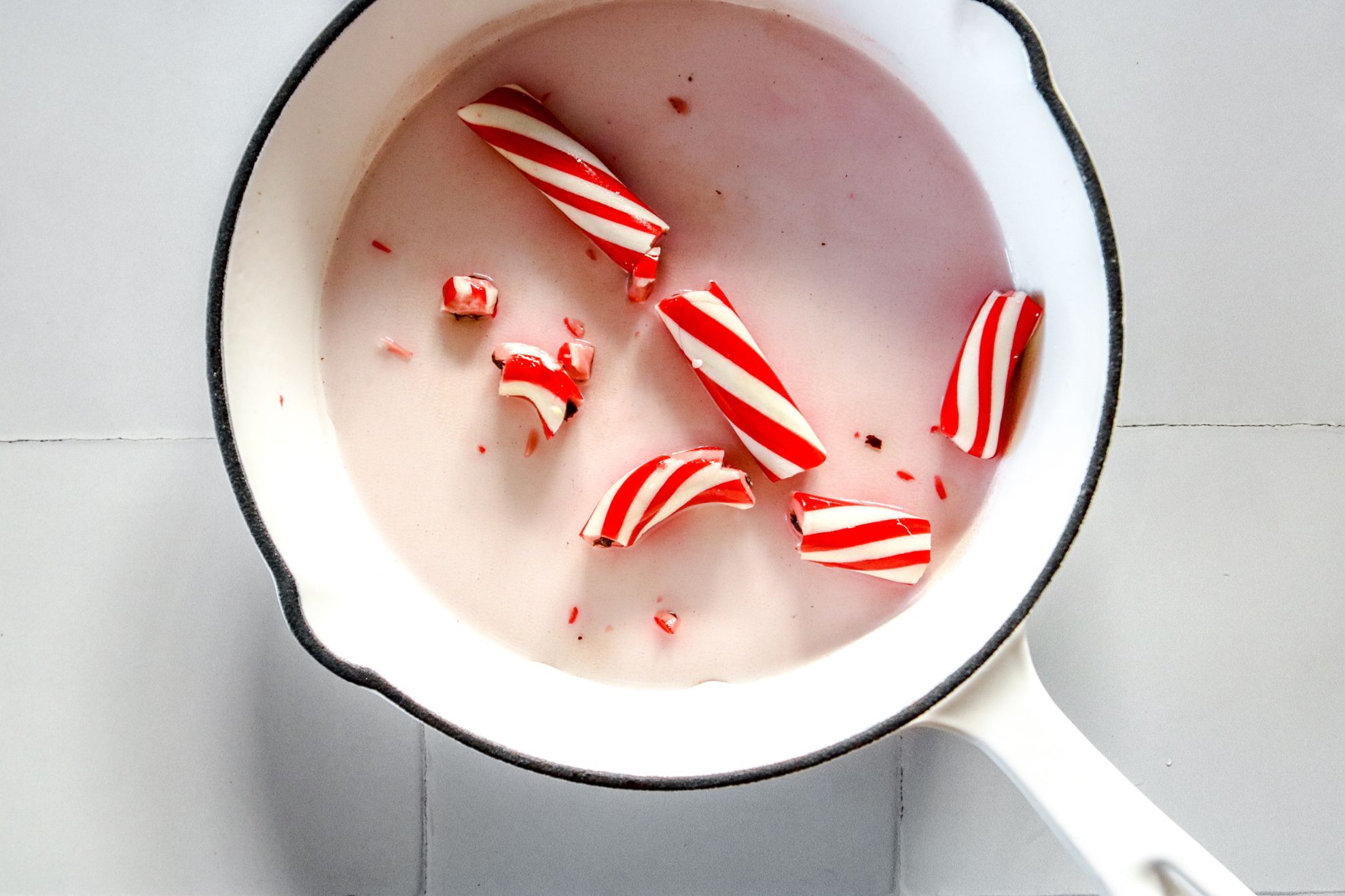 This is an overhead horizontal image of a white pan with broken up candy canes in it and some water. The pan sits on a white square tile surface.