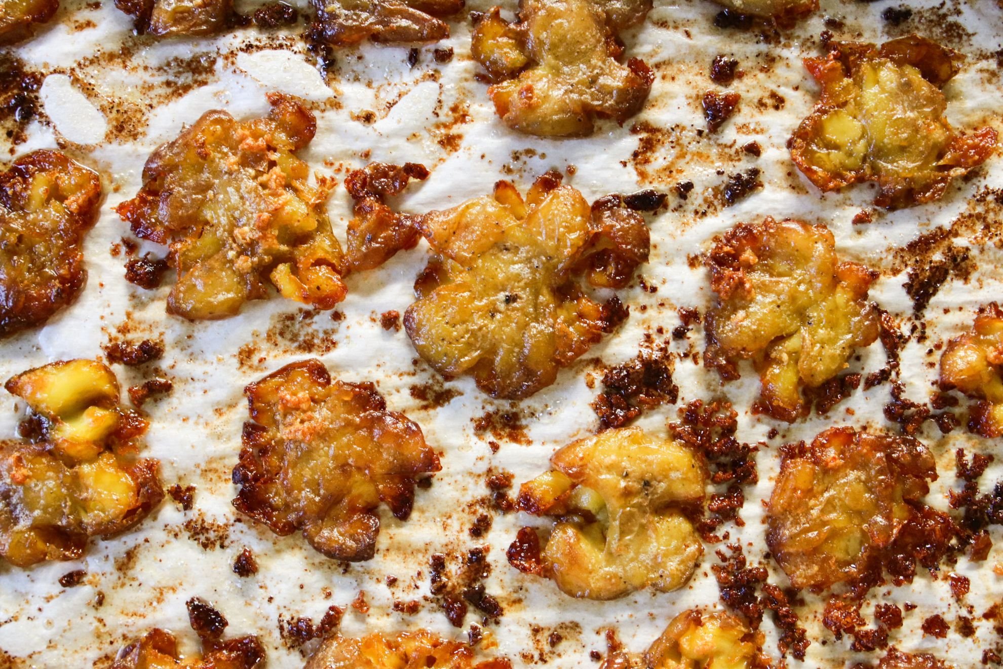 This is an overhead horizontal image of crispy roasted smashed potatoes on a white piece of parchment paper.