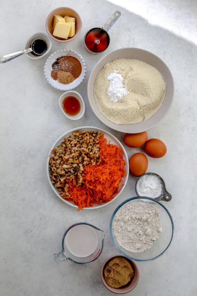 This is an overhead vertical image of ingredients to make carrot cake in individual bowls on a light grey surface.
