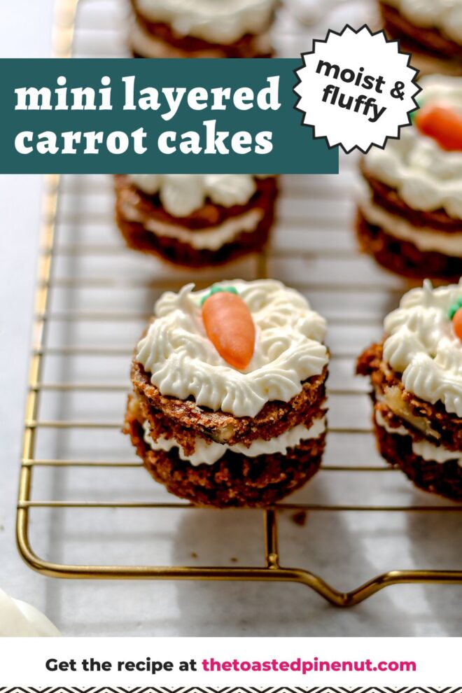 This is a vertical image of mini layered carrot cakes on a cooling rack. The cooling rack sits on a white surface. The cakes have a layer of cream cheese frosting in the middle and frosting on the top with a candy carrot. The image focuses on on cake but more are blurred around the cake on the cooling rack. Text overlay reads "mini layered carrot cakes moist & fluffy."