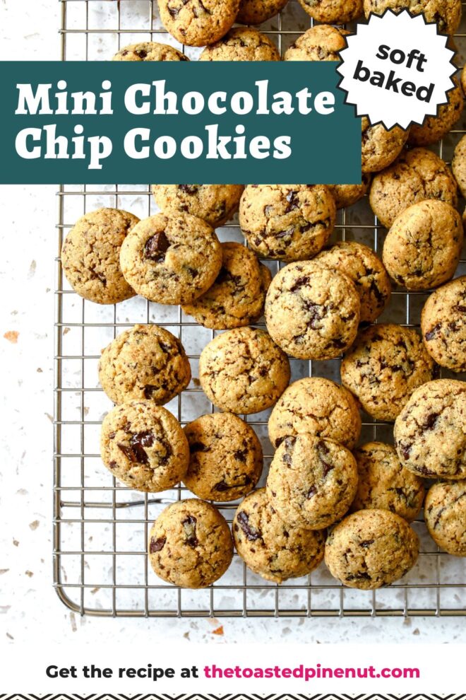 This is an overhead vertical image of a silver cooling rack with mini chocolate chip cookies piled on top. The image focuses on the bottom left corner of the cooling rack with the rest of the cooling rack out of frame. The cooling rack sits on a white terrazzo surface. Text overlay reads "soft baked mini chocolate chip cookies."
