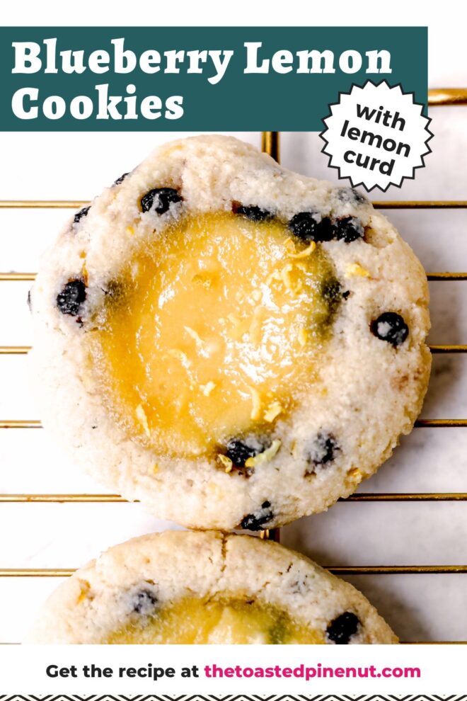 This is an overhead vertical image focusing close up on a cookie on a gold cooling rack with cookies on it. The cookies are studded with blueberries and have a lemon curd pool in the middle. The cooling rack is in a light grey surface. Text overlay reads "blueberry lemon cookies with lemon curd."